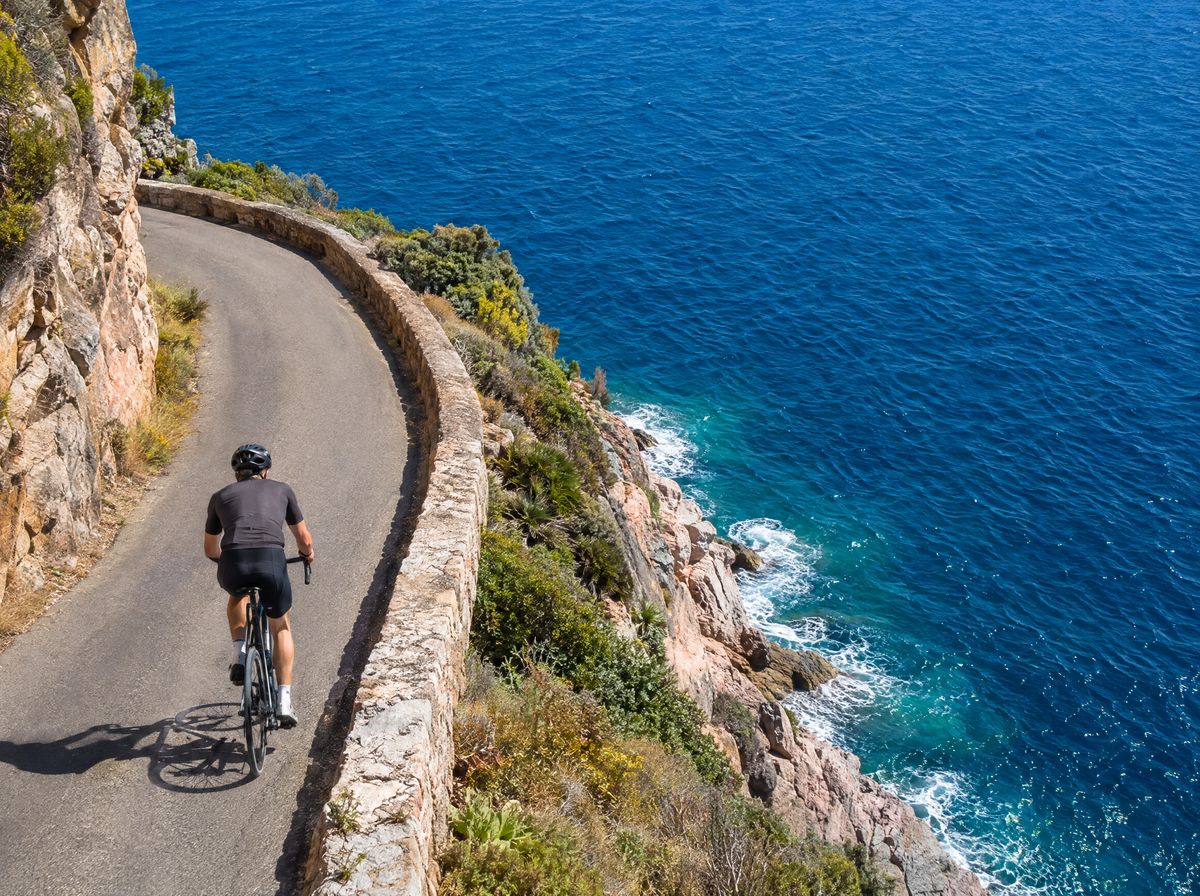 Cyclist on a coastal road carved into the cliff, with the sea below