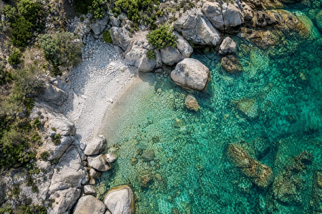 Granite cove with white pebbles and crystal-clear water, seen from above