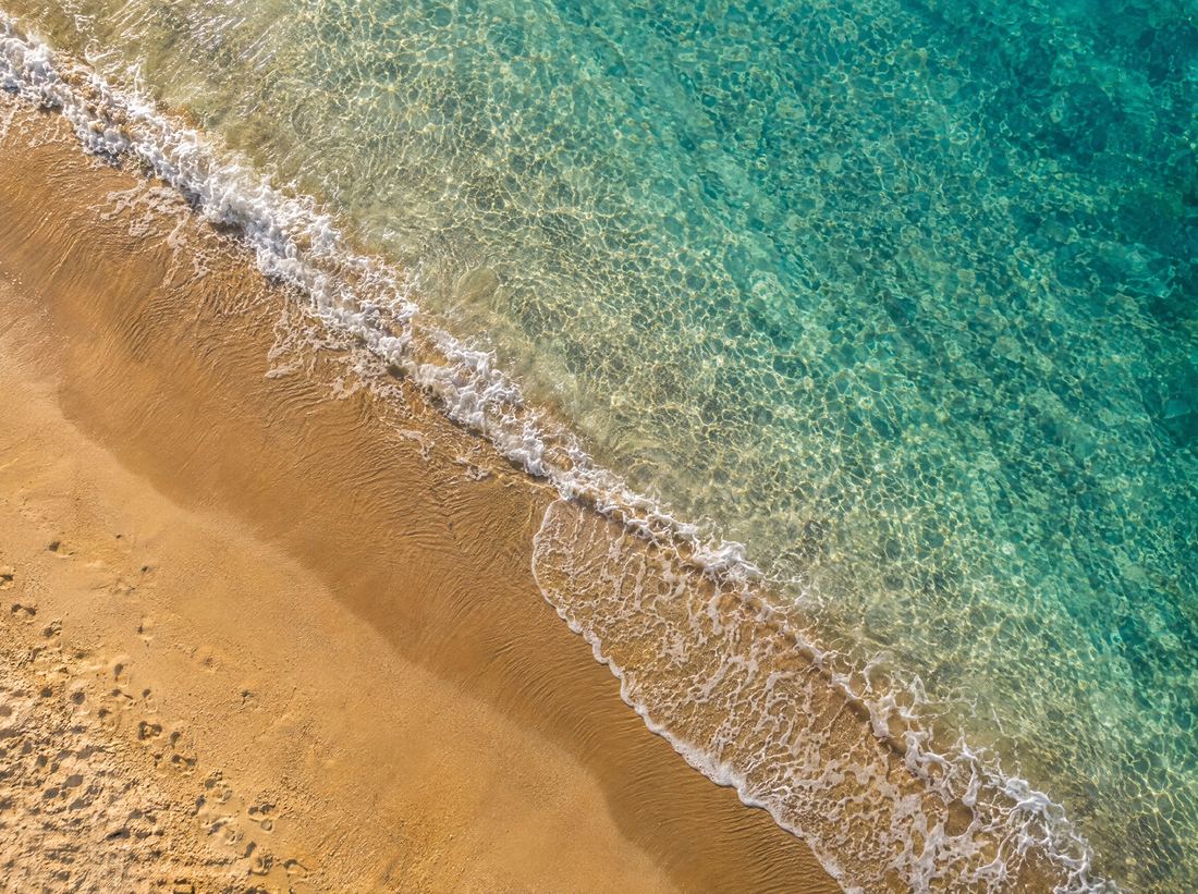 Golden sand shoreline with a gentle wave, seen from above