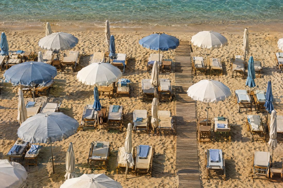 Beach umbrellas and sunbeds of a beach club on the sand, seen from above